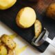 Close-up of potatoes and peeler on a cutting board, ready for cooking.