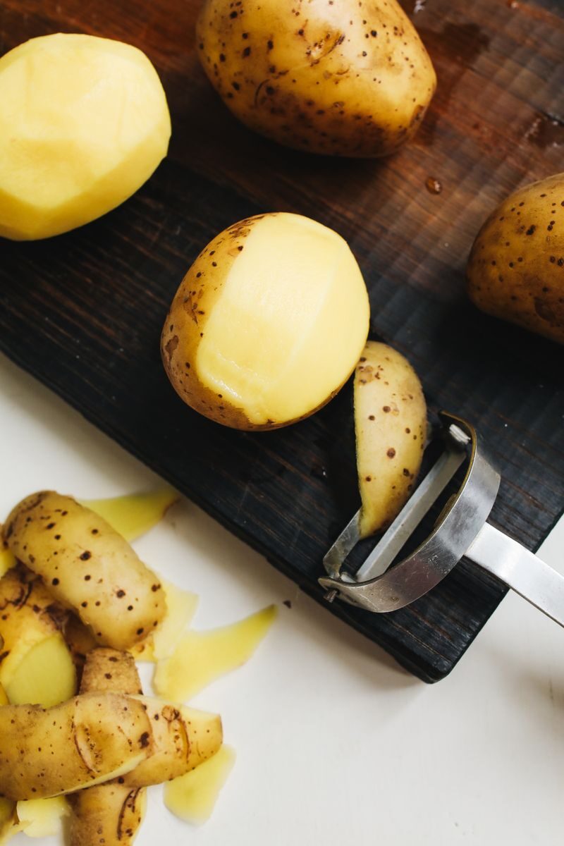 Close-up of potatoes and peeler on a cutting board, ready for cooking.