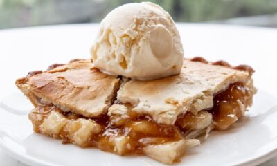 Piece of homemade apple pie served with scoop of vanilla ice cream on plate on white table