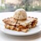 Piece of homemade apple pie served with scoop of vanilla ice cream on plate on white table
