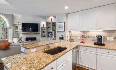 A modern kitchen with granite countertops opens into a stylish living room, featuring elegant furniture and built-in shelves.
