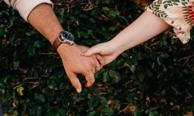 A close-up of a couple holding hands against a leafy background, symbolizing connection.