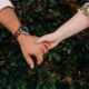 A close-up of a couple holding hands against a leafy background, symbolizing connection.