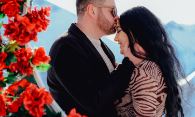 A couple shares a tender moment surrounded by vibrant red roses, creating a romantic atmosphere.