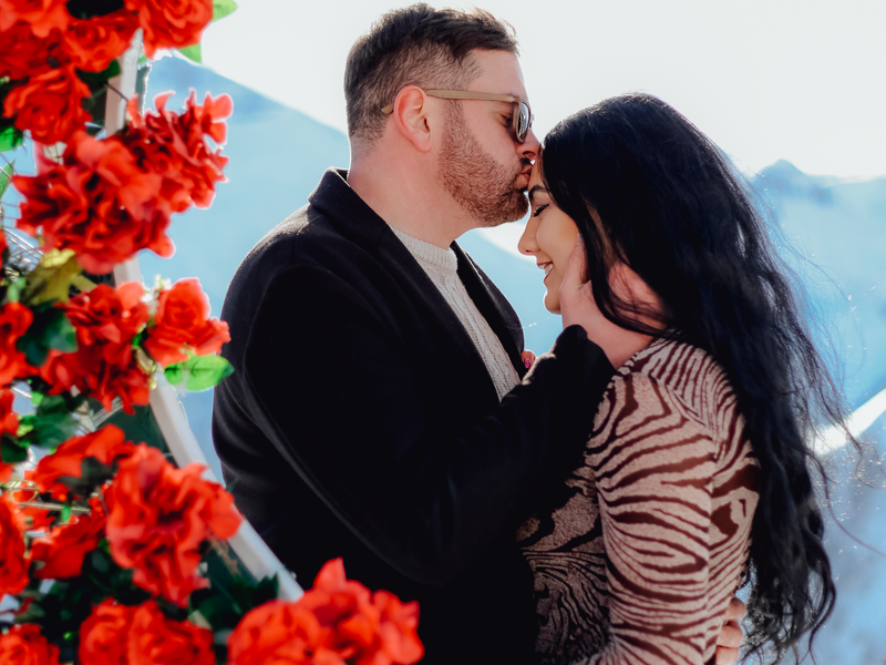 A couple shares a tender moment surrounded by vibrant red roses, creating a romantic atmosphere.