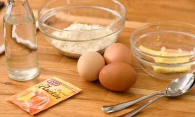 A variety of baking ingredients including flour, eggs, butter, and baking powder on a wooden table.