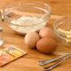 A variety of baking ingredients including flour, eggs, butter, and baking powder on a wooden table.