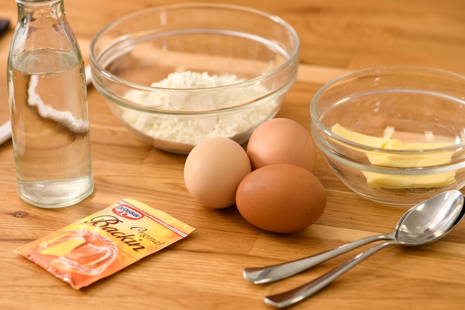 A variety of baking ingredients including flour, eggs, butter, and baking powder on a wooden table.