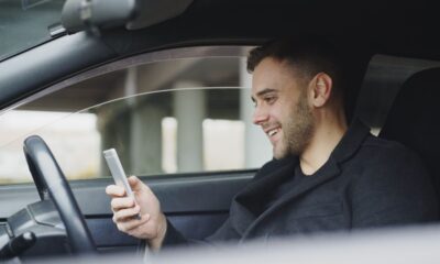 Adult man smiling while using a smartphone inside a car. Relaxed and happy expression.