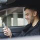 Adult man smiling while using a smartphone inside a car. Relaxed and happy expression.