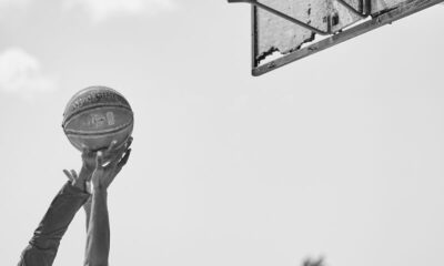 Two athletes compete for a basketball in an outdoor court in a dynamic black and white shot.