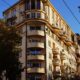 A classic architectural residential building with balconies in a city setting under a clear blue sky.