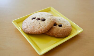 Two freshly baked chocolate chip cookies served on a yellow plate.