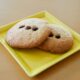 Two freshly baked chocolate chip cookies served on a yellow plate.