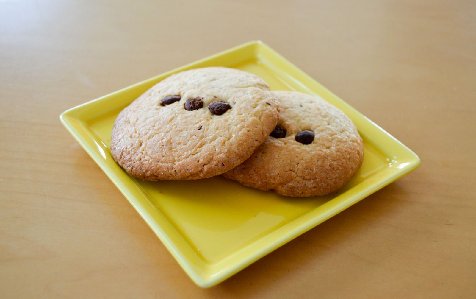 Two freshly baked chocolate chip cookies served on a yellow plate.