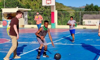 A group of teenagers enjoying a lively game on an outdoor basketball court under the bright summer sun.