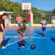 A group of teenagers enjoying a lively game on an outdoor basketball court under the bright summer sun.