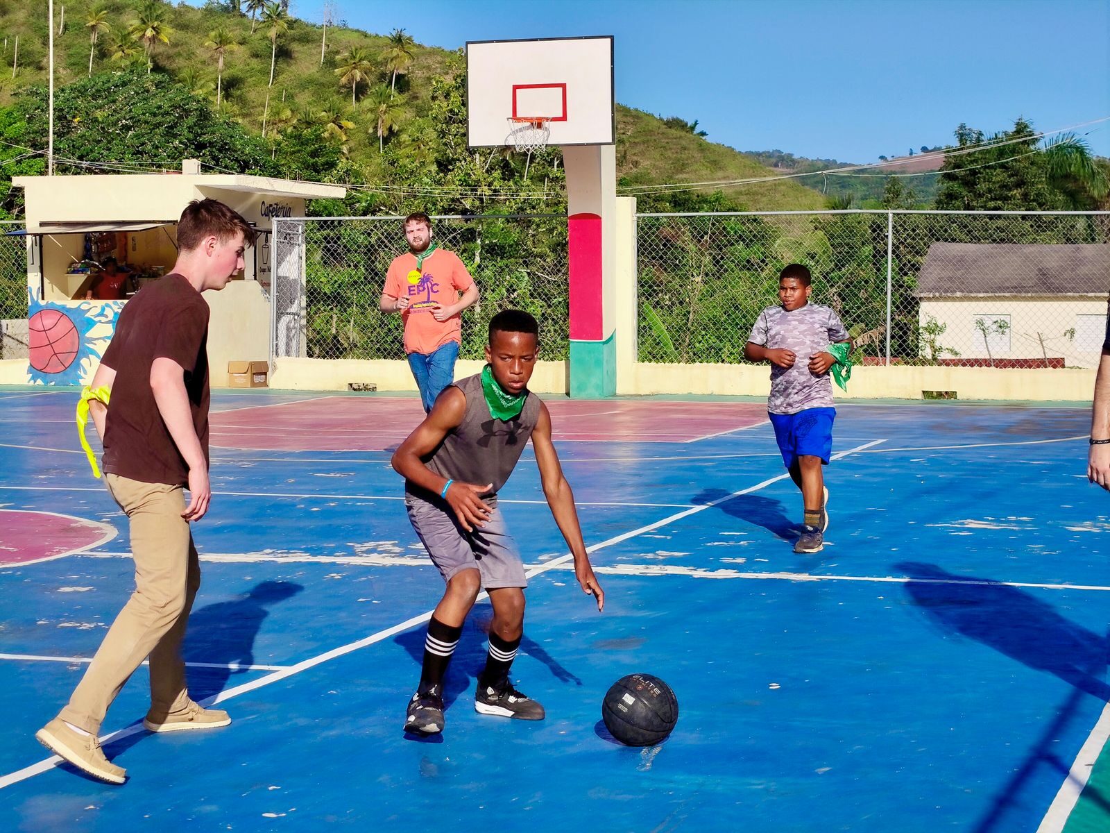 A group of teenagers enjoying a lively game on an outdoor basketball court under the bright summer sun.
