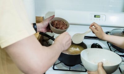 Close-up view of hands adding ingredients into pot on stove, preparing a meal.