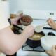 Close-up view of hands adding ingredients into pot on stove, preparing a meal.