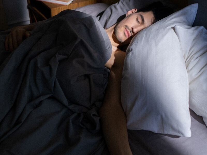 A man sleeps peacefully in a sunlit bedroom, with soft shadows cast on his face.