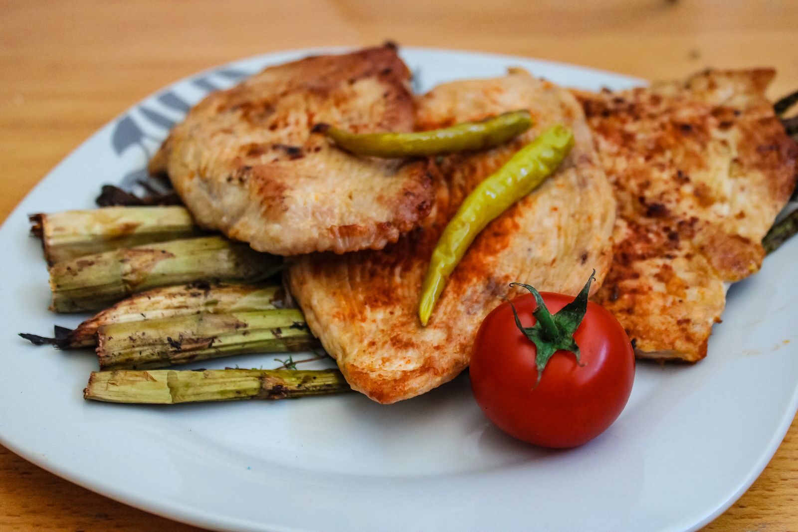 A savory plate of grilled chicken with asparagus and a fresh tomato.