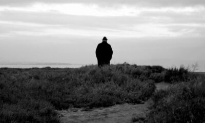 A solitary figure walking along a coastal path under a cloudy sky, captured in monochrome.