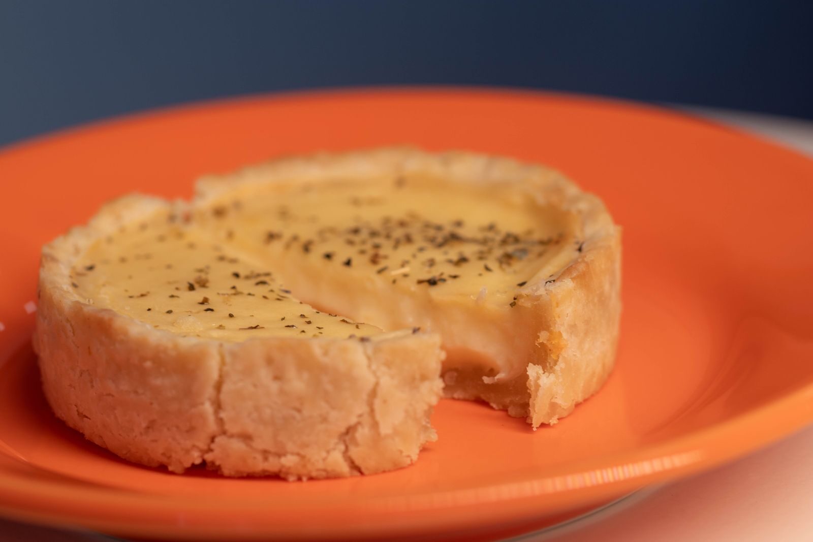 Close-up of a savory quiche with herbs on a vibrant orange plate.