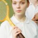 Portrait of a young woman in sportswear holding a vintage tennis racket, looking confident and focused.