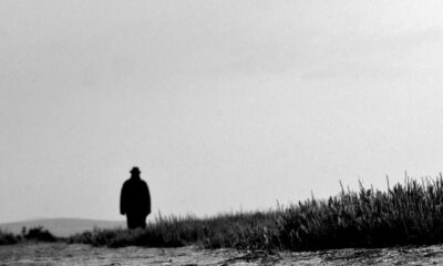 A solitary silhouette stands on a gravel path under an overcast sky, evoking solitude and mystery.
