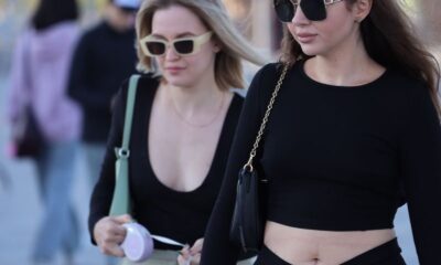 Two stylish women in black outfits and sunglasses walking outdoors on a sunny day.