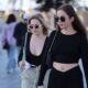 Two stylish women in black outfits and sunglasses walking outdoors on a sunny day.