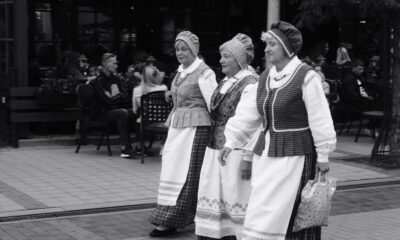 Three women in traditional Lithuanian costumes walking in a street parade downtown.