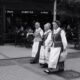 Three women in traditional Lithuanian costumes walking in a street parade downtown.