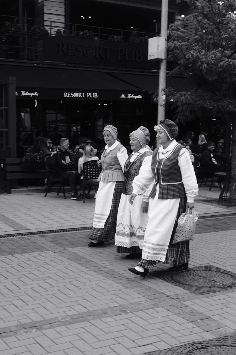 Three women in traditional Lithuanian costumes walking in a street parade downtown.