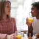 Two women enjoying a casual conversation while drinking orange juice in a café.