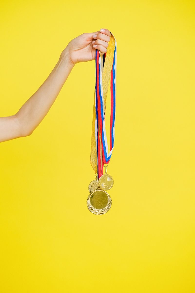 A hand holding multiple gold medals with colorful ribbons on a vibrant yellow background.