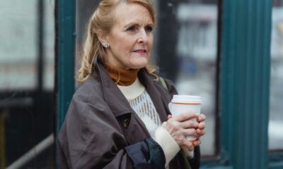 Contemplative elderly female in outerwear with hot beverage to go looking forward in town in daylight