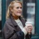 Contemplative elderly female in outerwear with hot beverage to go looking forward in town in daylight
