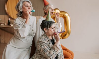 A joyful celebration with senior women in party hats blowing party blowers indoors.