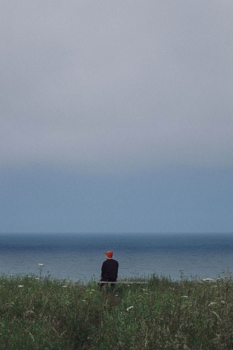 A lone person sits on a bench gazing at the serene ocean horizon, encapsulating solitude and tranquility.