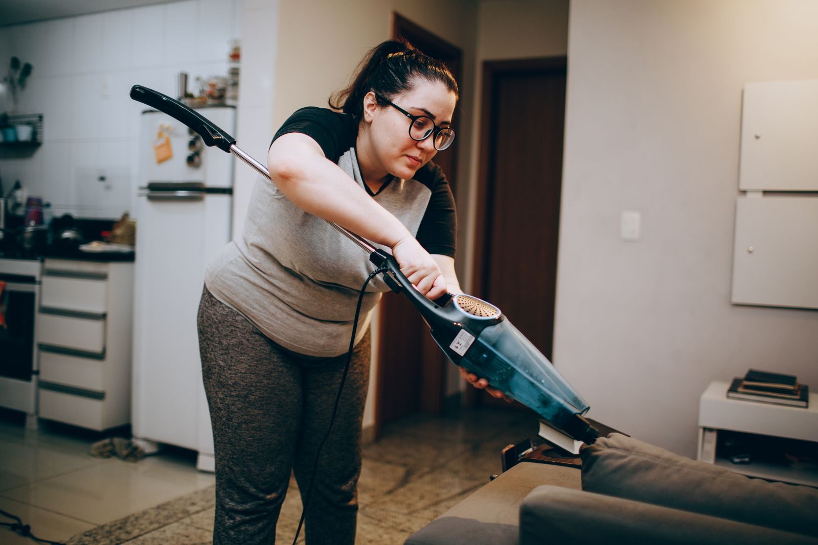 A woman vacuuming a couch in a cozy living room setting, emphasizing daily housework.
