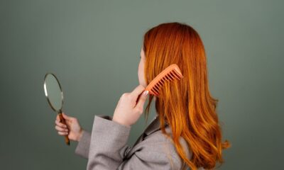 Red-haired woman using a comb while holding a mirror, focusing on hair care and beauty.