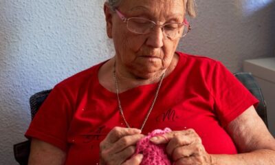 Senior woman in red shirt knitting pink yarn indoors, focusing on craft.