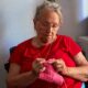Senior woman in red shirt knitting pink yarn indoors, focusing on craft.