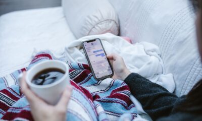Person relaxing indoors with coffee and smartphone, texting in a cozy setting.