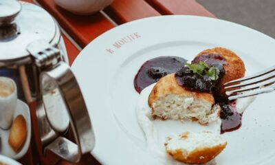 High-angle shot of syrniki with berry sauce on a table outdoors, surrounded by coffee and tea service.