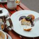 High-angle shot of syrniki with berry sauce on a table outdoors, surrounded by coffee and tea service.