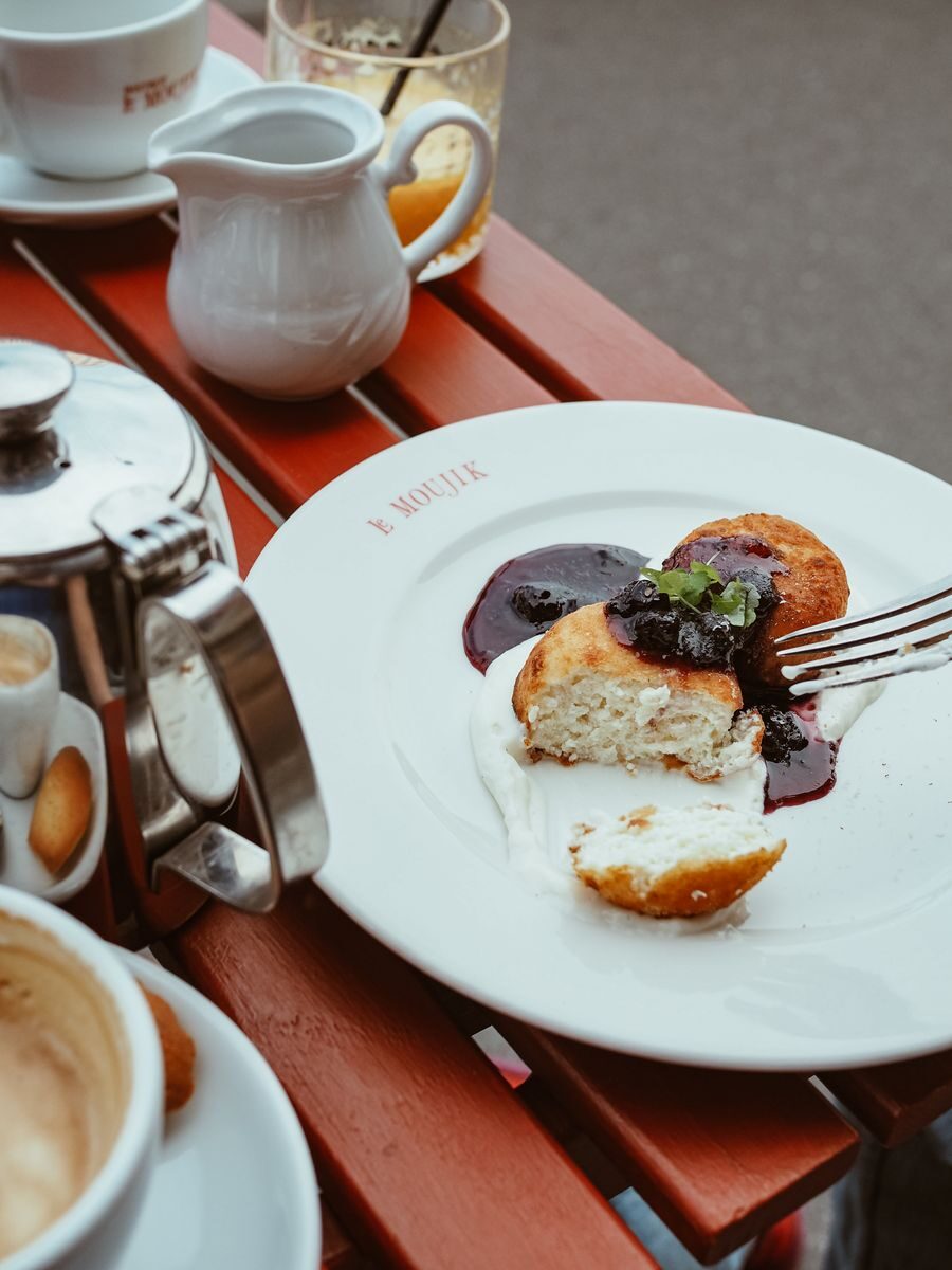 High-angle shot of syrniki with berry sauce on a table outdoors, surrounded by coffee and tea service.