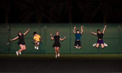 Group of teenagers jumping in celebration on an outdoor tennis court at night.